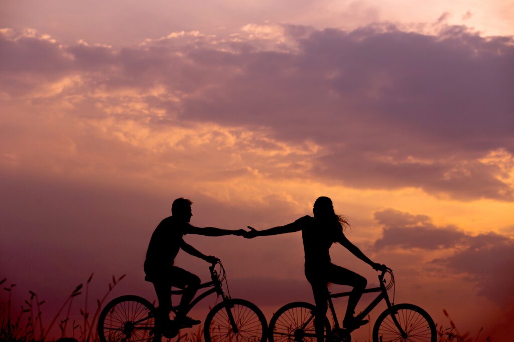 Woman on a bike reaching out hand to man behind her also on a bike
