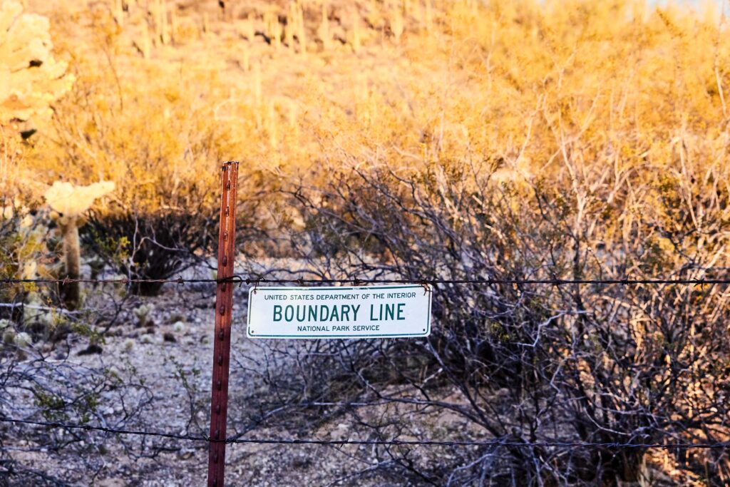 White and black boundary line sign on a fence with rough ground behind