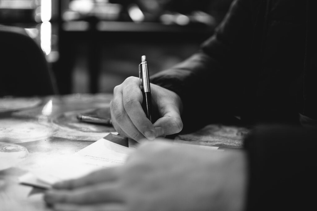 A person writing a list on a piece of paper, in black and white