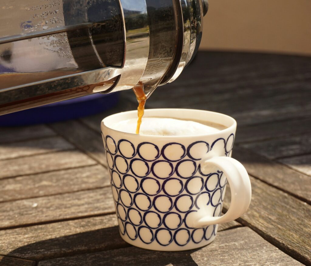 Close-up of a cafetiere being poured into a white and black ceramic mug on a brown wooden table
