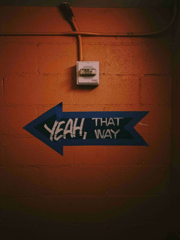 Blue arrow on an orange wall painted with the words “Yeah, that way”