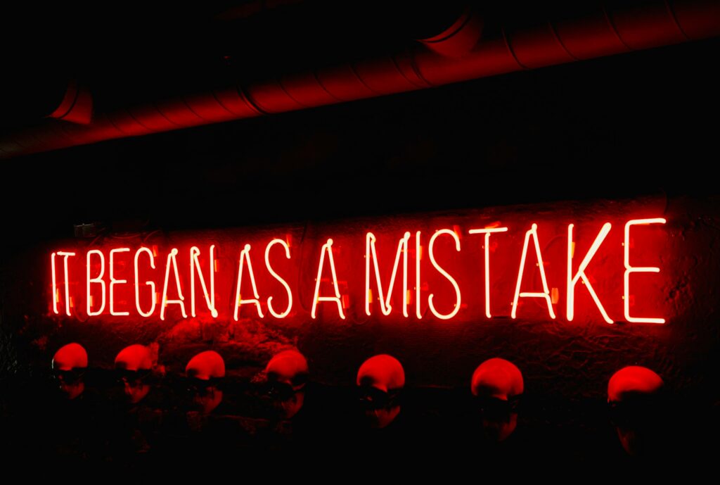 Red neon sign reading “it began as a mistake”
