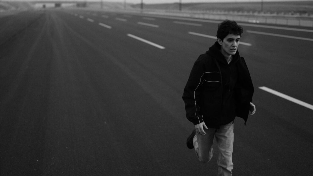 Man running down an empty motorway towards the camera, in black and white Photo by lhon karwan