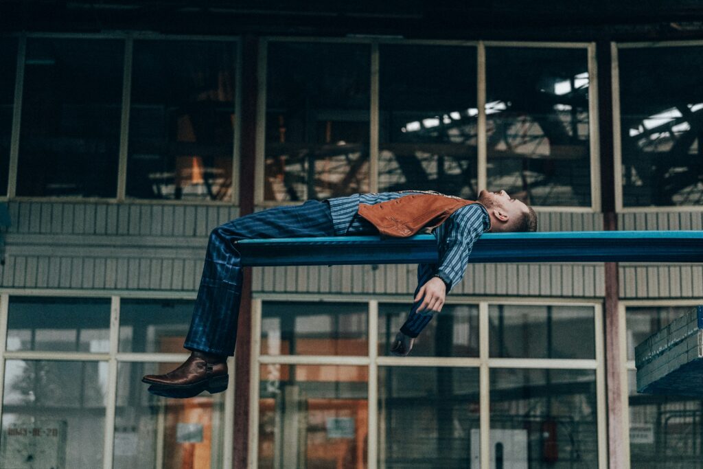 Man laying exhausted on a blue bench in front of a building Photo by Vitalii Khodzinskyi on Unsplash